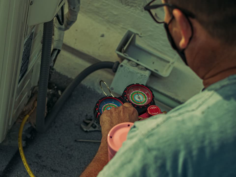 Técnico conectando manómetros a una unidad exterior de aire acondicionado