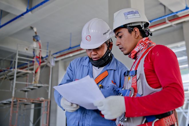 Dos ingenieros con casco revisan planos en una obra